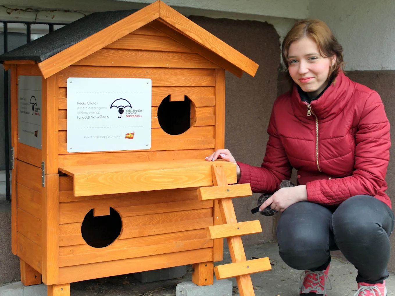 Wolontariuszka fundacji przy drewnianym domku Kocia Chata dla kotów wolno żyjących